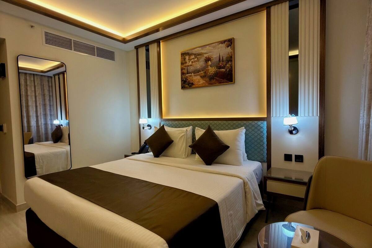 A hotel room with a large bed, a desk, a chair, a painting on the wall, and a mirror.