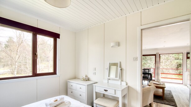 A bedroom with a bed, a dresser, a vanity with a mirror, and a view of an outdoor balcony. - Beautiful 4 star, 2 bedroom chalet with mountain views. A true Highland landscape all around (Crianlarich)
