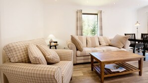 A living room with a sofa, armchair, coffee table, and a lamp. - Beautiful 4 star, 2 bedroom chalet with mountain views. A true Highland landscape all around (Crianlarich)