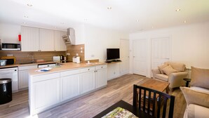 A modern kitchen with white cabinets, a microwave, and a sink. There is a dining area with a table and chairs, and a sofa. - Beautiful 4 star, 2 bedroom chalet with mountain views. A true Highland landscape all around (Crianlarich)