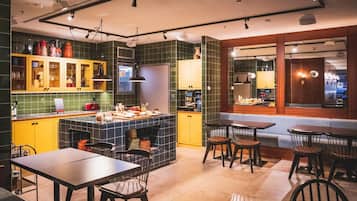 Une cuisine moderne avec des meubles de couleur jaune, un îlot central et un coin repas doté de tables et de chaises en bois.