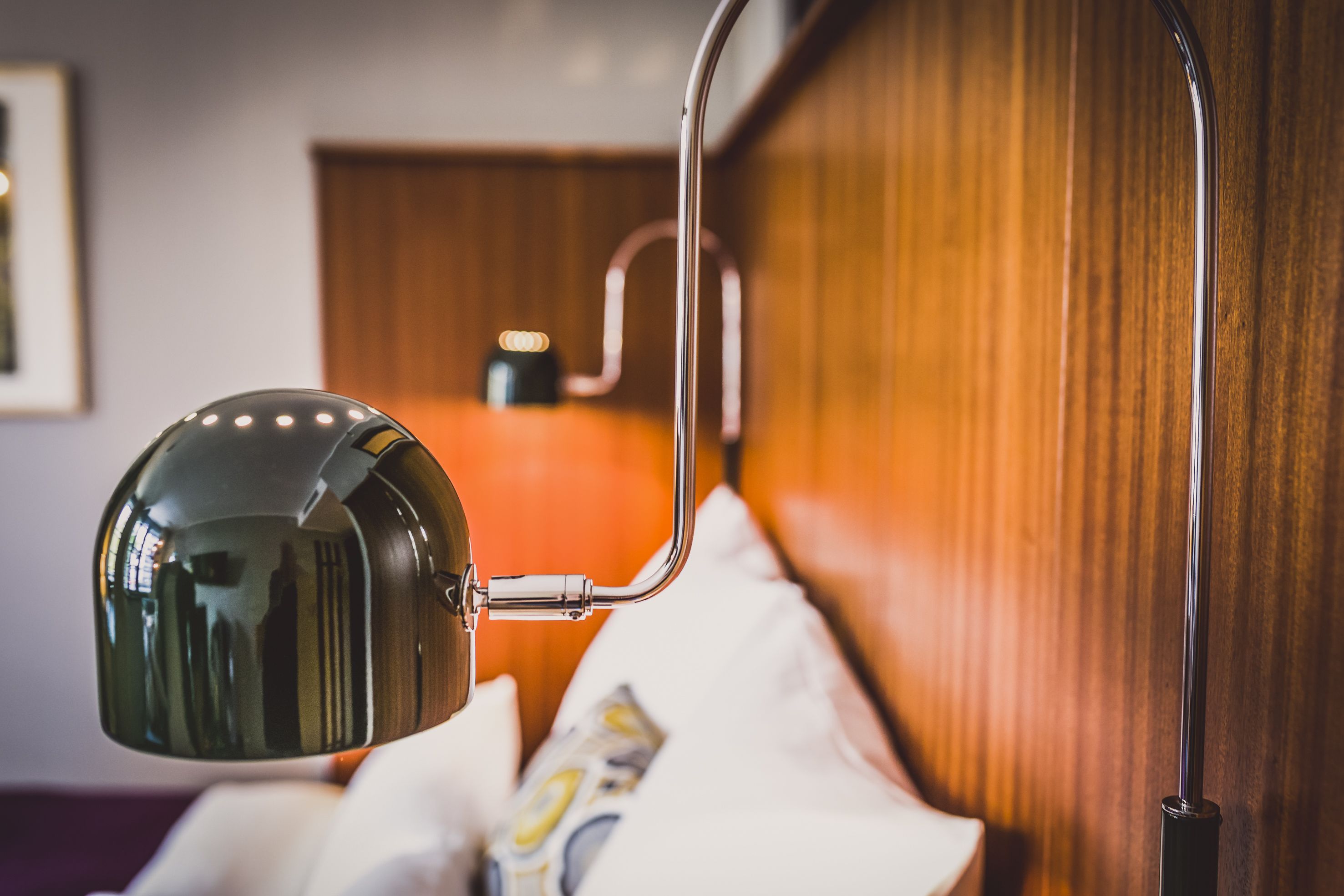 Detalle de un rincón de habitación con una cama, cabecera de madera y una lámpara de pared.