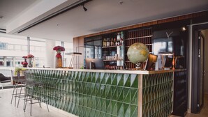 A modern bar area with a green-tiled partition, a globe, and various bottles. - HENRI Hotel Düsseldorf (Düsseldorf)