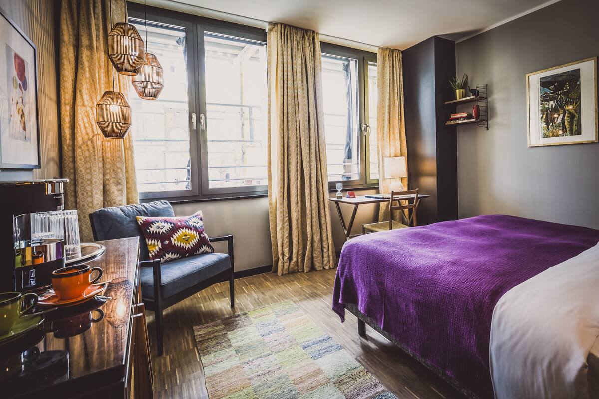 Une chambre d’hôtel comprenant un lit, un bureau, une chaise, une fenêtre avec des rideaux et une vue sur l’extérieur.