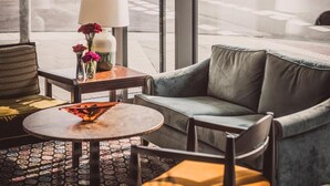 A modern hotel lobby with a large window offering a view of the street. Inside, there is a comfortable seating area with a sofa and chairs, a small table with a lamp, and a vase with flowers. - HENRI Hotel Düsseldorf (Düsseldorf)