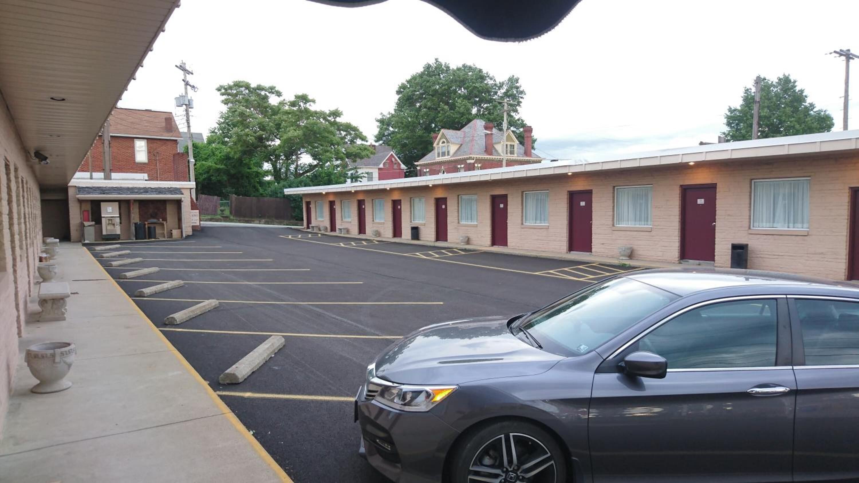 A parking lot with a row of single-story motel rooms, a car parked in front, and a building with a cross on top.