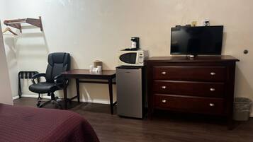 A hotel room with a bed, a desk with a chair, a microwave, a small refrigerator, a dresser, and a television.