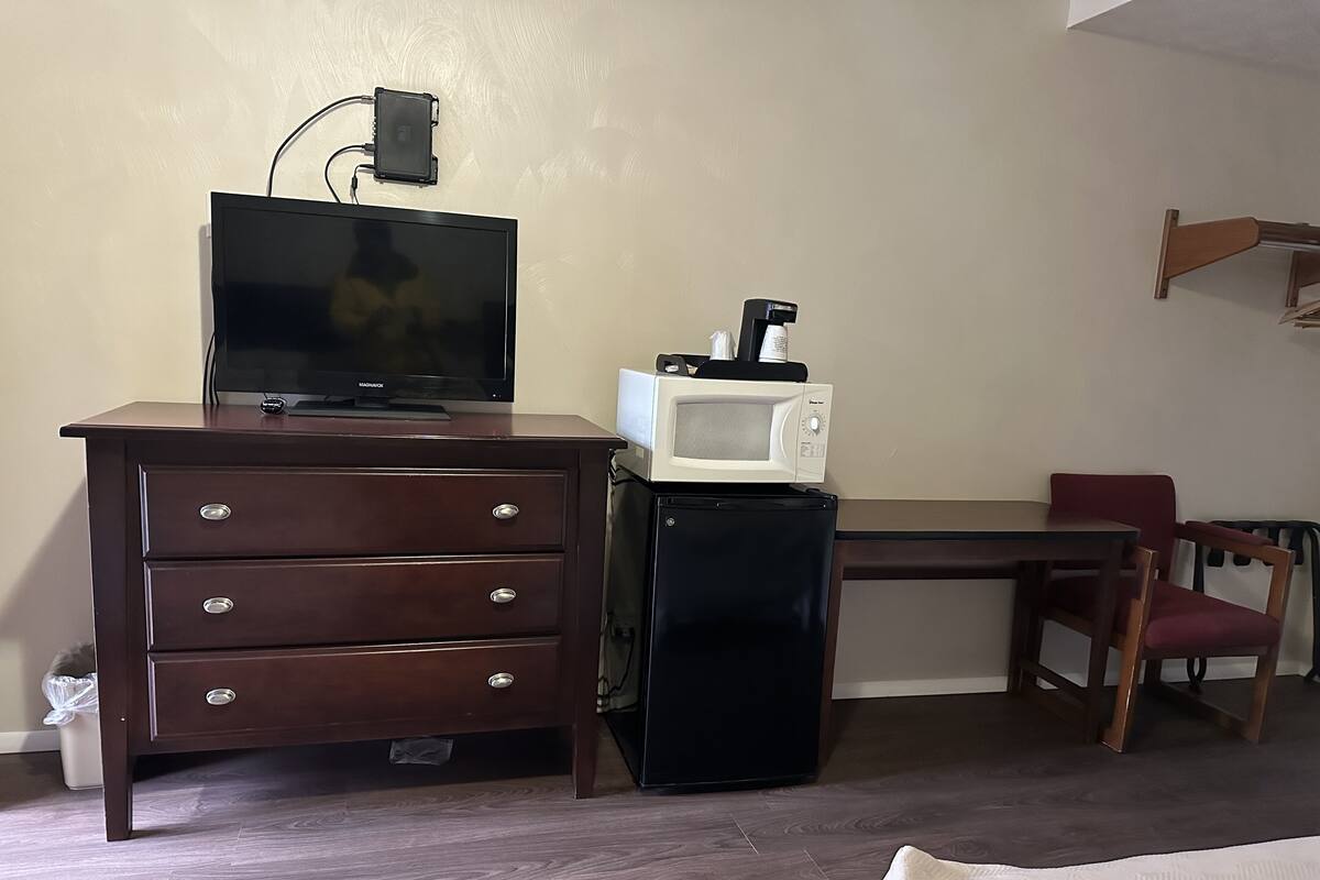 A room with a wooden dresser, a television, a microwave, and a small refrigerator.