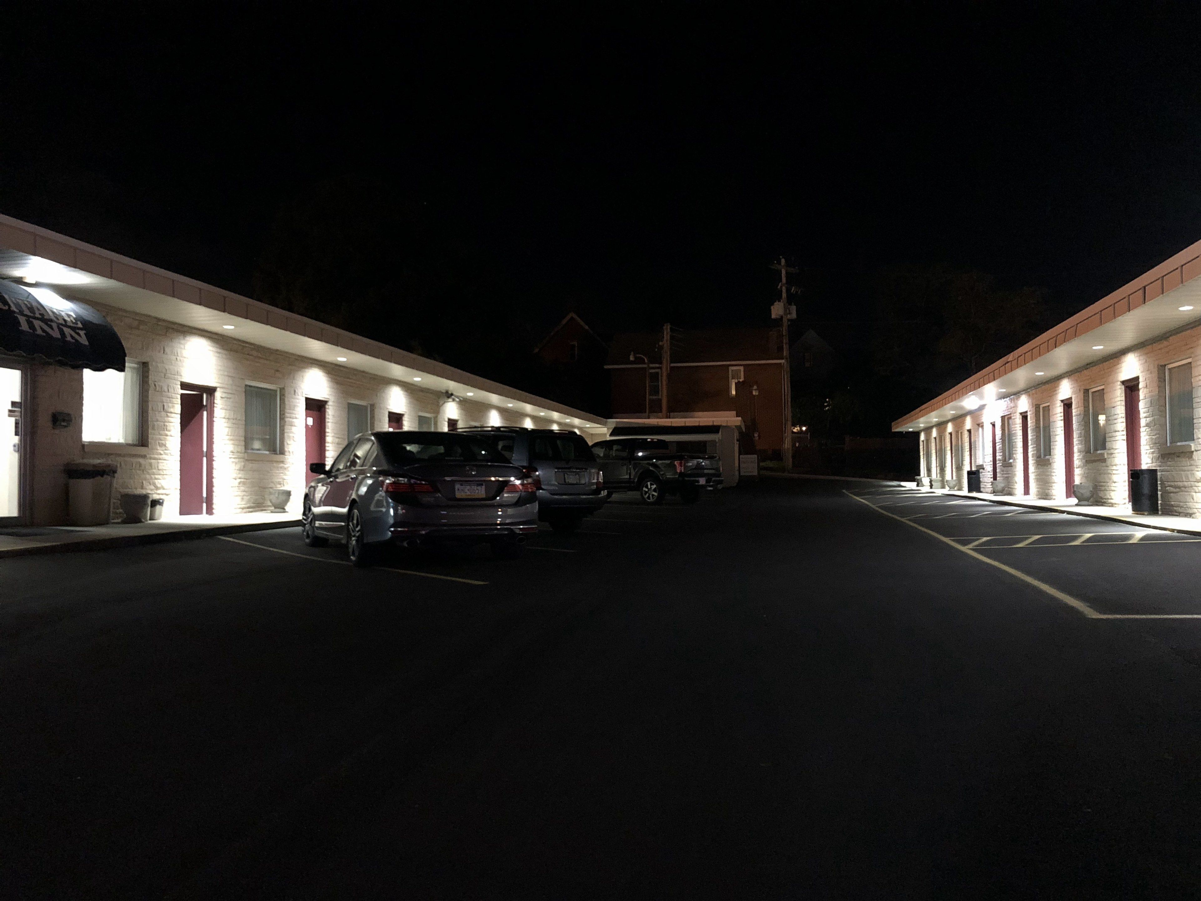 Ein Motel mit einer Reihe von Zimmern, einem Parkplatz und einem Gebäude im Hintergrund.