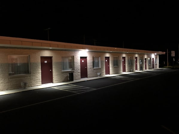 Uma fileira de quartos de motel, cada um com porta e janela individual, iluminados por uma única luz.