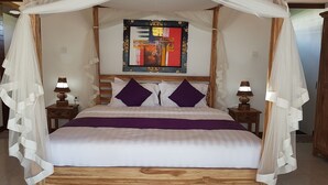 A four-poster canopy bed with a wooden headboard, two nightstands with lamps, and a colorful abstract painting above the bed. - Buda Cottage Ubud (Ubud)