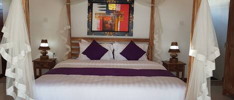 A four-poster canopy bed with a wooden headboard, two nightstands with lamps, and a colorful abstract painting above the bed.