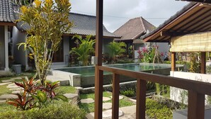 A pool area with a stone deck, surrounded by tropical plants and a traditional tiled roof structure. - Buda Cottage Ubud (Ubud)