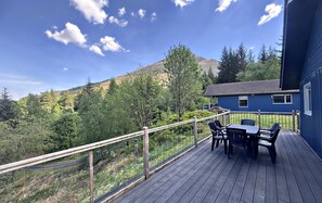 Une terrasse avec une table et des chaises, donnant sur une zone boisée avec une montagne en arrière-plan.