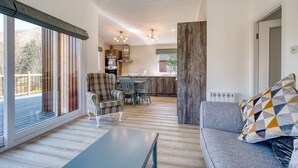 Een ruime woonkamer met een bank, een salontafel en een eettafel met stoelen. Achtergrond is een keuken zichtbaar, en een groot raam biedt uitzicht op de omgeving.
