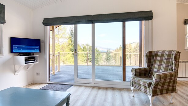 Een kamer met een televisie, een geruit fauteuil en een schuifdeur naar een balkon.