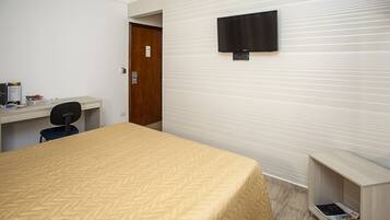 A hotel room with a bed, a desk, a chair, a television mounted on the wall, and a door.