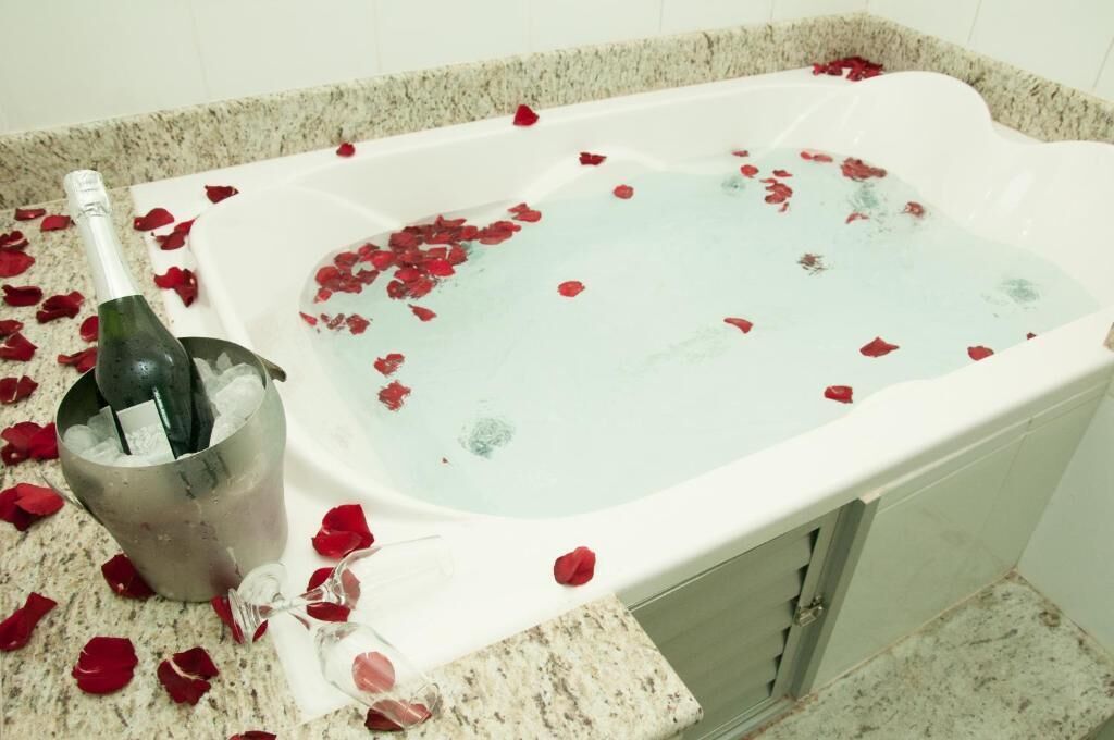 A bathtub filled with water and rose petals, a bottle of champagne, and a glass in a metal bucket.