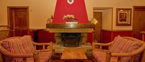 Una habitación acogedora con dos sillones de mimbre, una mesita de madera y una chimenea roja con un escudo decorativo.