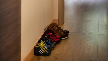 A hallway with a coat rack holding a yellow jacket, a pair of skis, and a pair of hiking boots. There is a chair and a table with a window in the background.