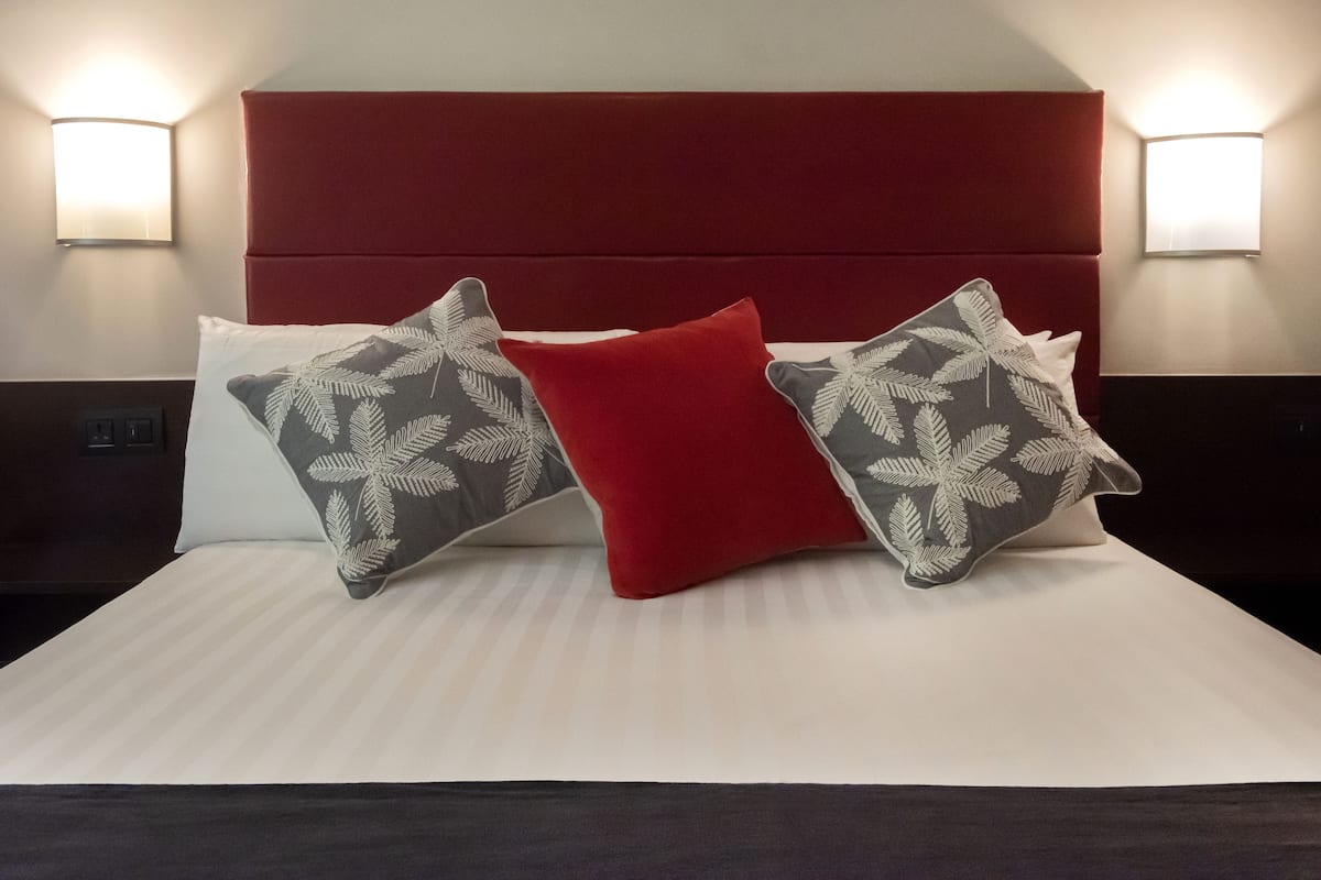 A neatly made bed with a red headboard, two patterned pillows, and two wall-mounted lights.