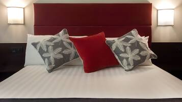 Een net opgemaakt bed met een rode hoofdbord, twee gestreepte kussens en twee wandlampen.