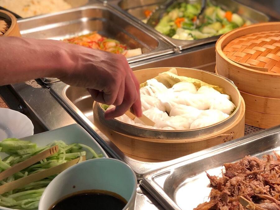 Buffet com diversas opções de comida, incluindo um prato de dumplings, um guisado de carne desfiada e uma xícara de café.