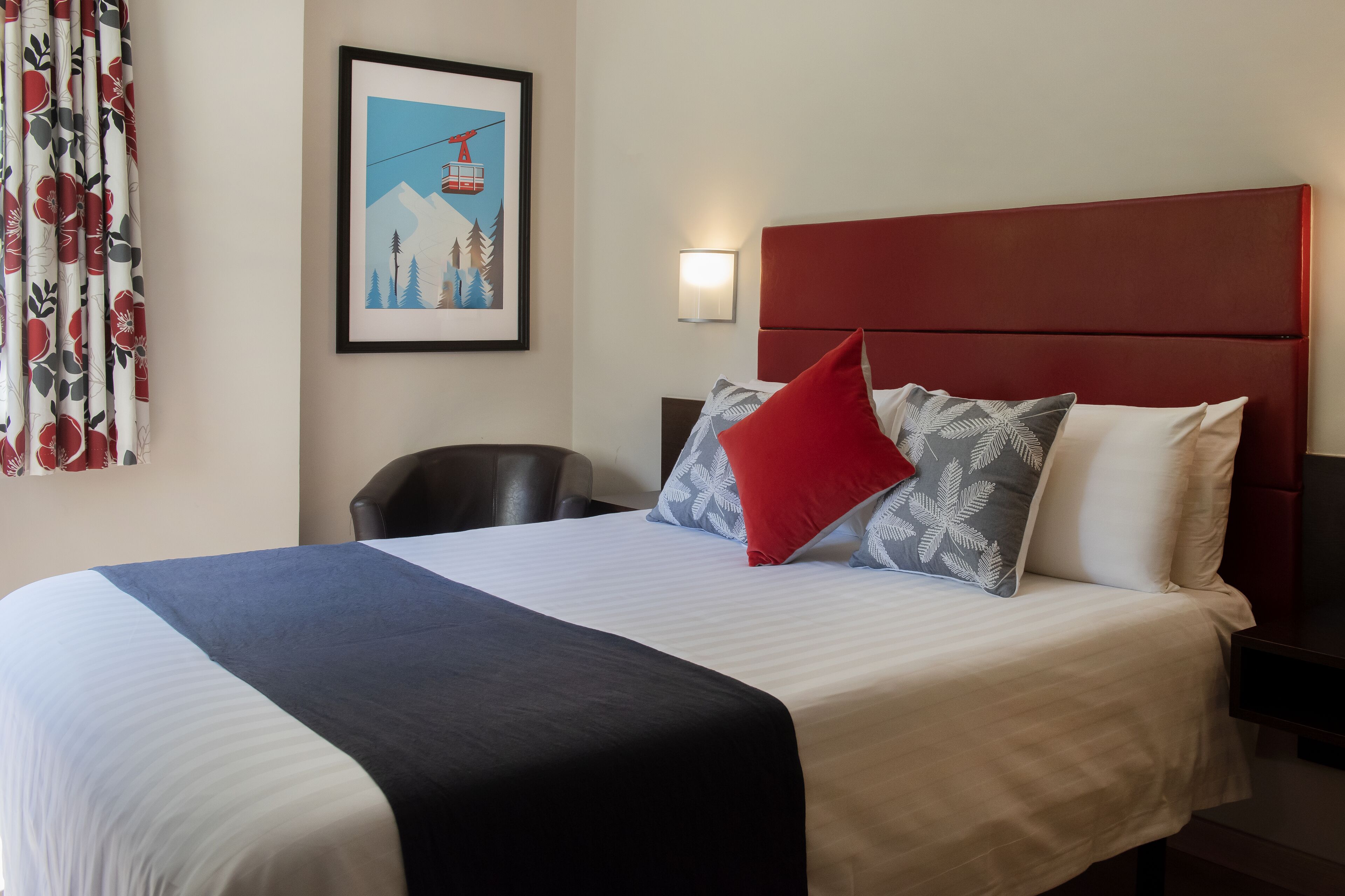 A hotel room with a large bed, a red headboard, and a framed picture on the wall.