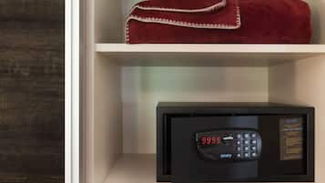 A black safe with a digital display and keypad, placed on a white shelf above a folded red towel.