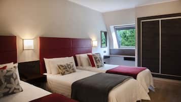 Quarto de hotel com duas camas, cabeceira vermelha, uma janela grande e vista para o verde lá fora.