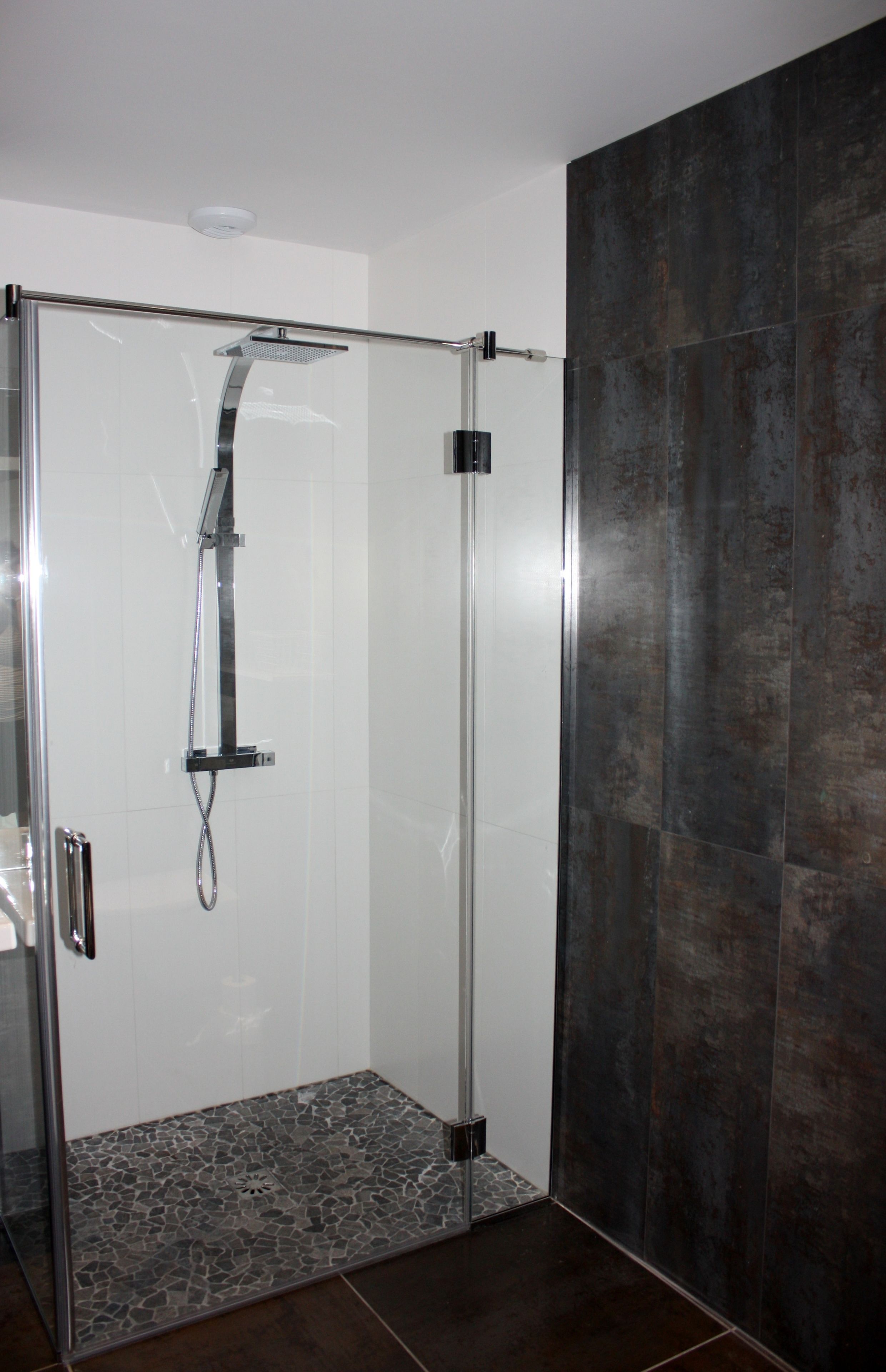 A glass-enclosed shower with a handheld showerhead and a wall-mounted control panel.