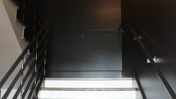 A staircase with a handrail, a light fixture, and an exit sign.