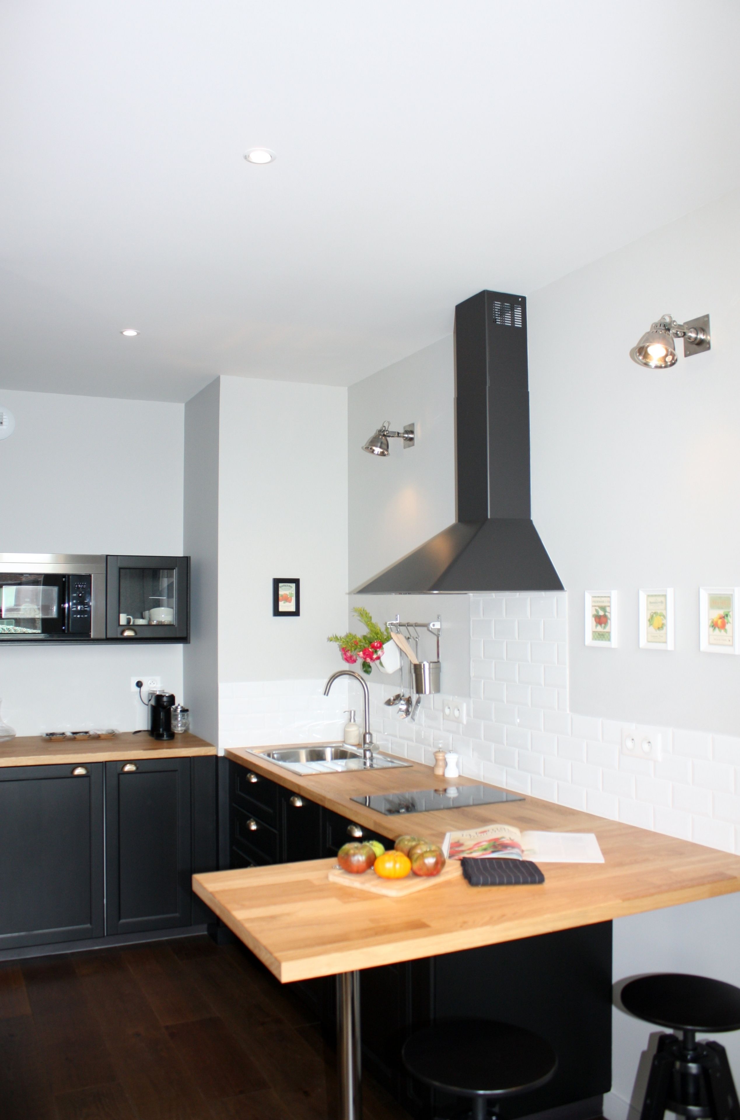 A modern kitchen with dark cabinetry, a wooden countertop, a stainless steel sink, and a black range hood.