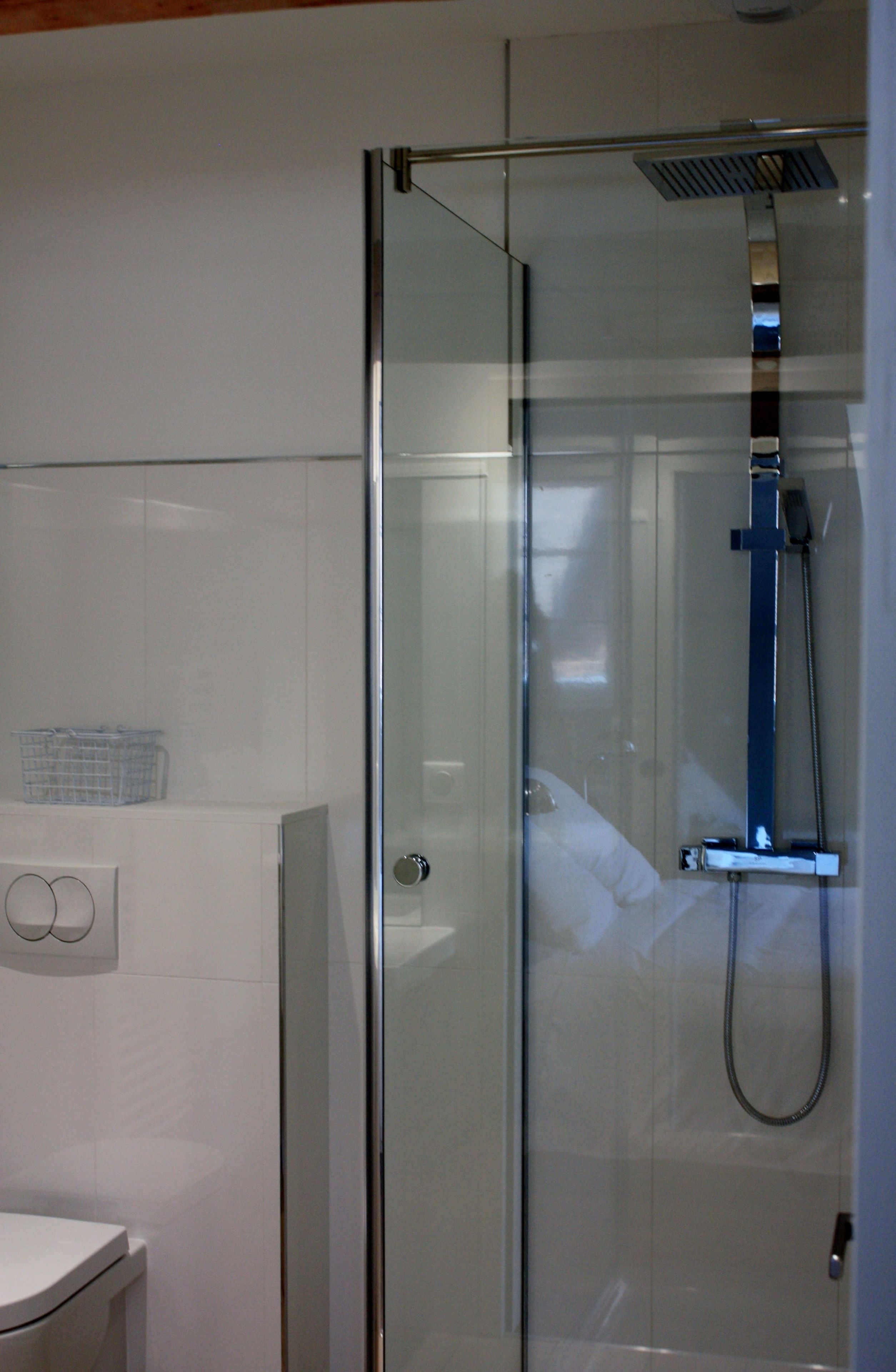 A glass-enclosed shower with a handheld showerhead and a wall-mounted control panel.