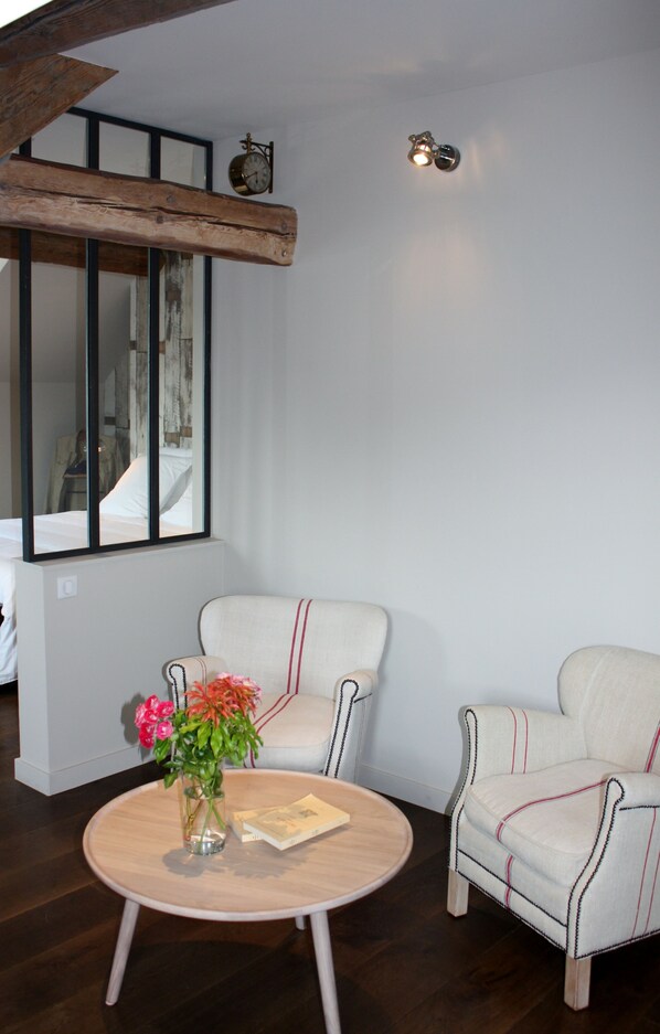 A room with a round wooden table, two upholstered chairs, a vase with flowers, and a bed with a white comforter. - Apparthôtels de Val-Perrière (Arbois)