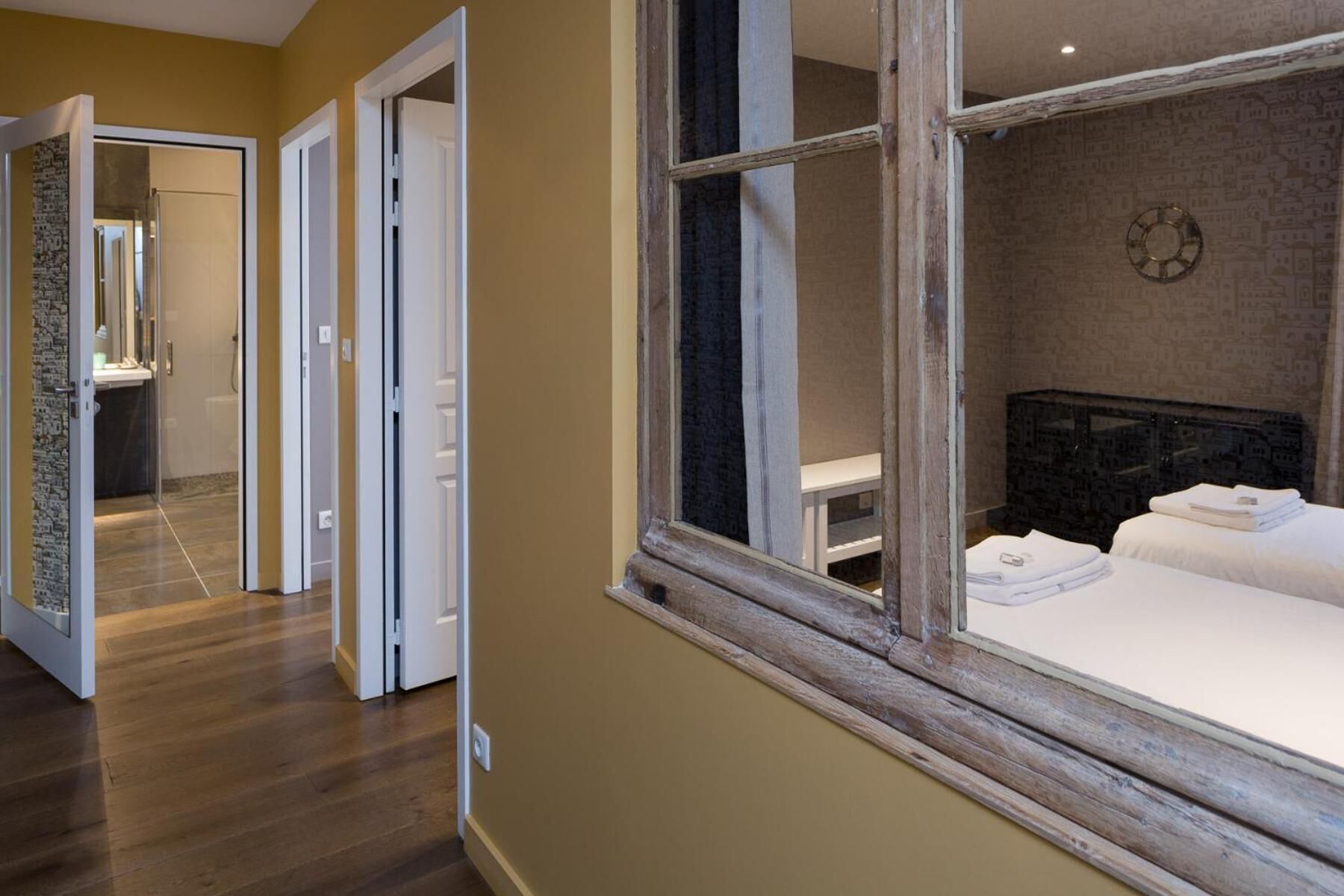 Habitación de hotel con un ventanal grande, una cama con ropa blanca impecable y un baño con ducha a la vista.