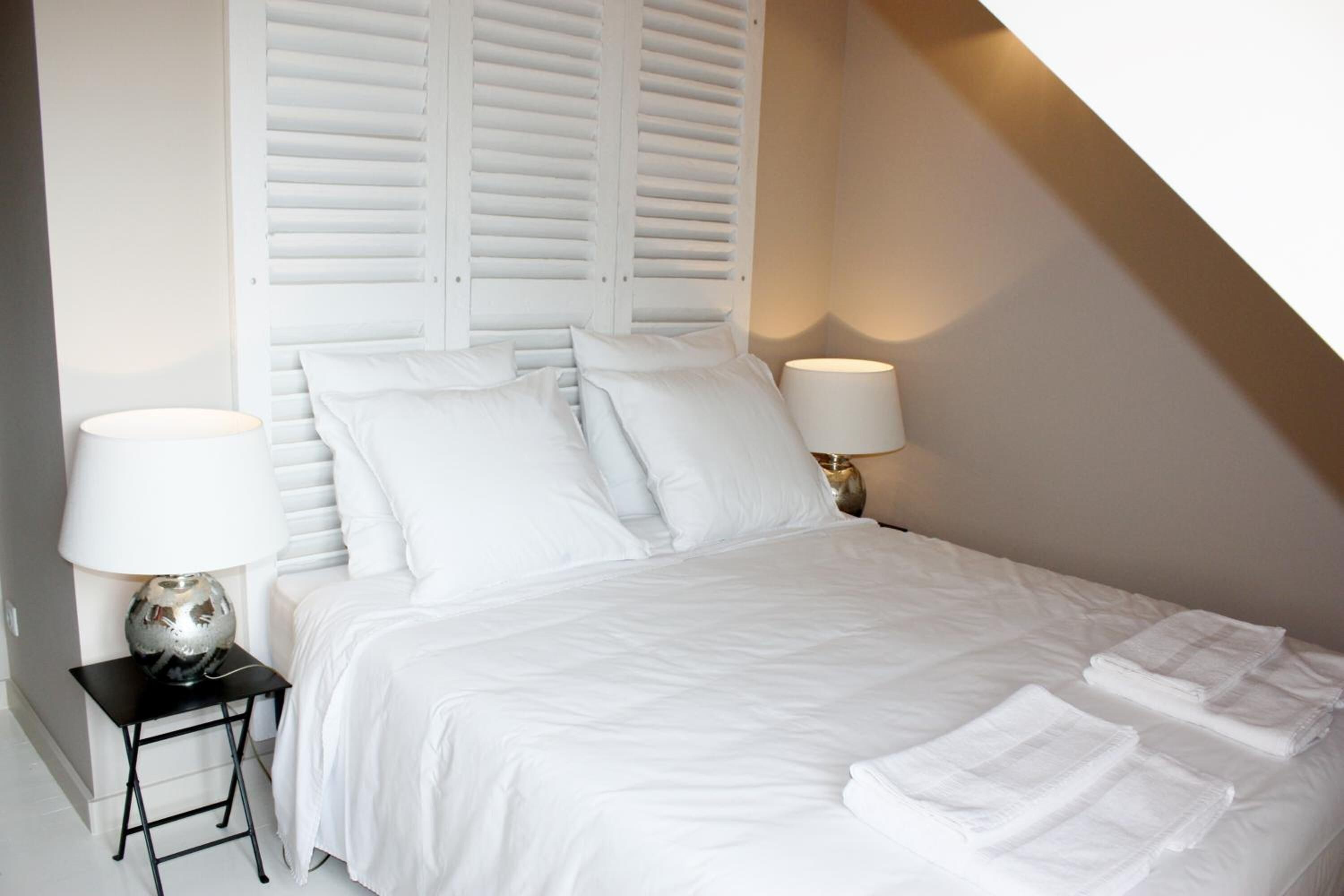 A neatly made bed with white linens and pillows, two bedside lamps, and a small table with a lamp.