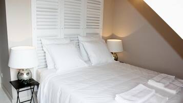 A neatly made bed with white linens and pillows, two bedside lamps, and a small table with a lamp.