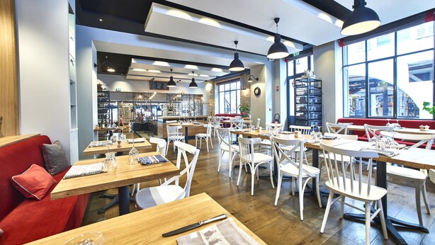 A spacious cafe with wooden tables and white chairs, large windows, and a modern interior design. - Apparthôtels de Val-Perrière (Arbois)