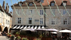 A stone building with a sign for 'DOCKS BRASSERIE' and outdoor seating with umbrellas. - Apparthôtels de Val-Perrière (Arbois)