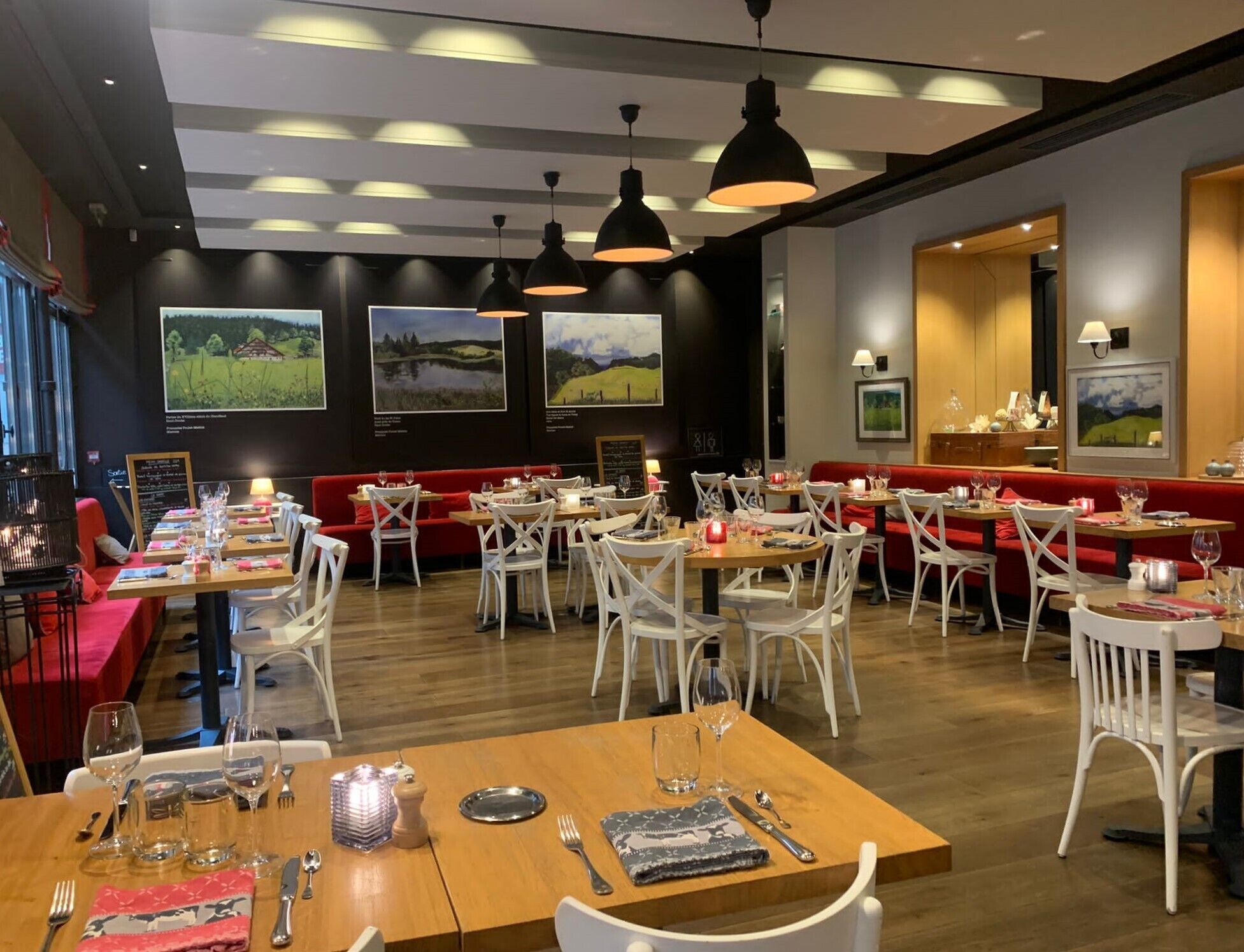 A restaurant with wooden tables and white chairs, red booths, and pendant lighting.