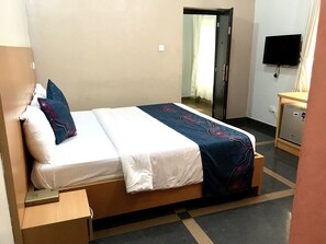 A hotel room with a bed, a nightstand, a desk, a television, and a wardrobe. - Beij-Inn & Suite Limited (Lagos)