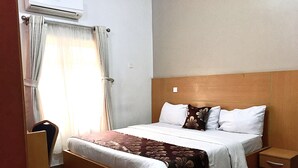Camera d'albergo con un letto in legno, biancheria bianca, una coperta a motivi marroni, un comodino e una sedia.