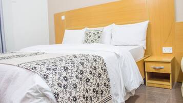 Een hotelkamer met een houten hoofdeinde, een bed met wit beddengoed, een bed met een gestreept plaid en een houten nachtkastje met een lade.