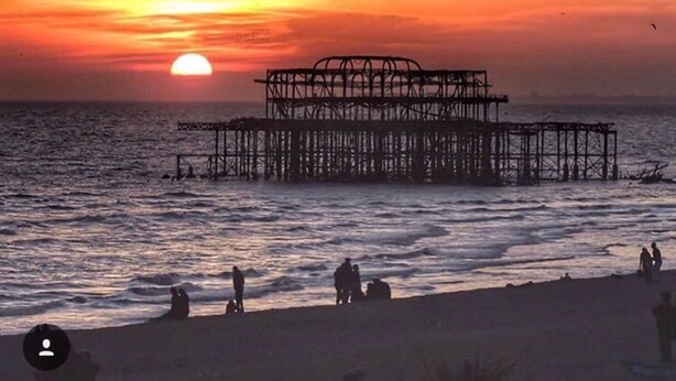 Un coucher de soleil sur une plage, avec une jetée en arrière-plan.