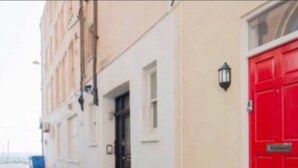 Une rue étroite avec une porte rouge et une petite plante en pot sur le trottoir.
