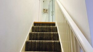 Un escalier recouvert d’une moquette à motifs, avec des murs blancs et une porte en verre en haut.