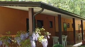 A covered outdoor area with a pergola, white plastic chairs, and a potted plant. - Camping Rio Verde (Costacciaro)
