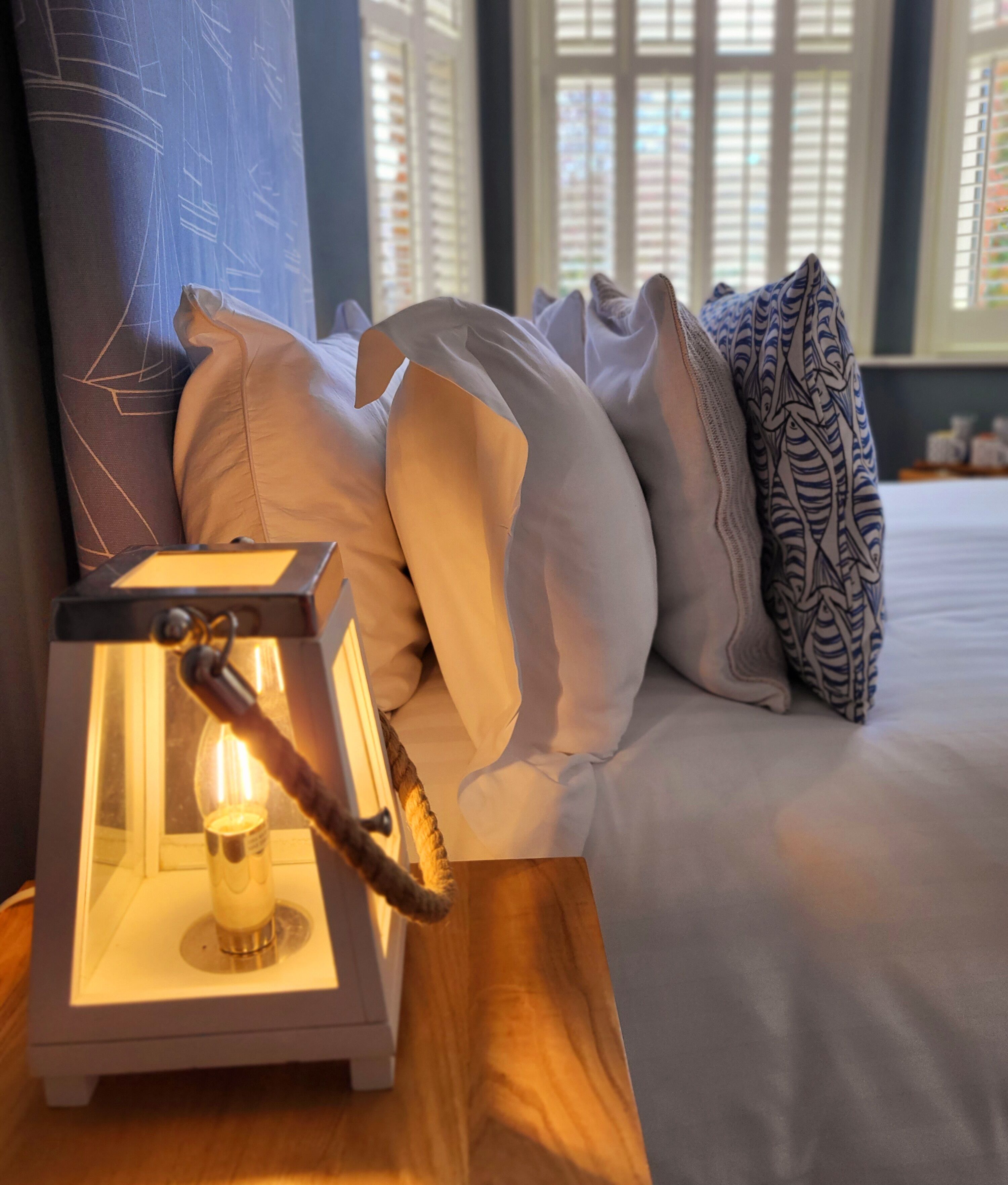 A neatly arranged bed with pillows, a bedside table with a lamp, and a window with blinds.