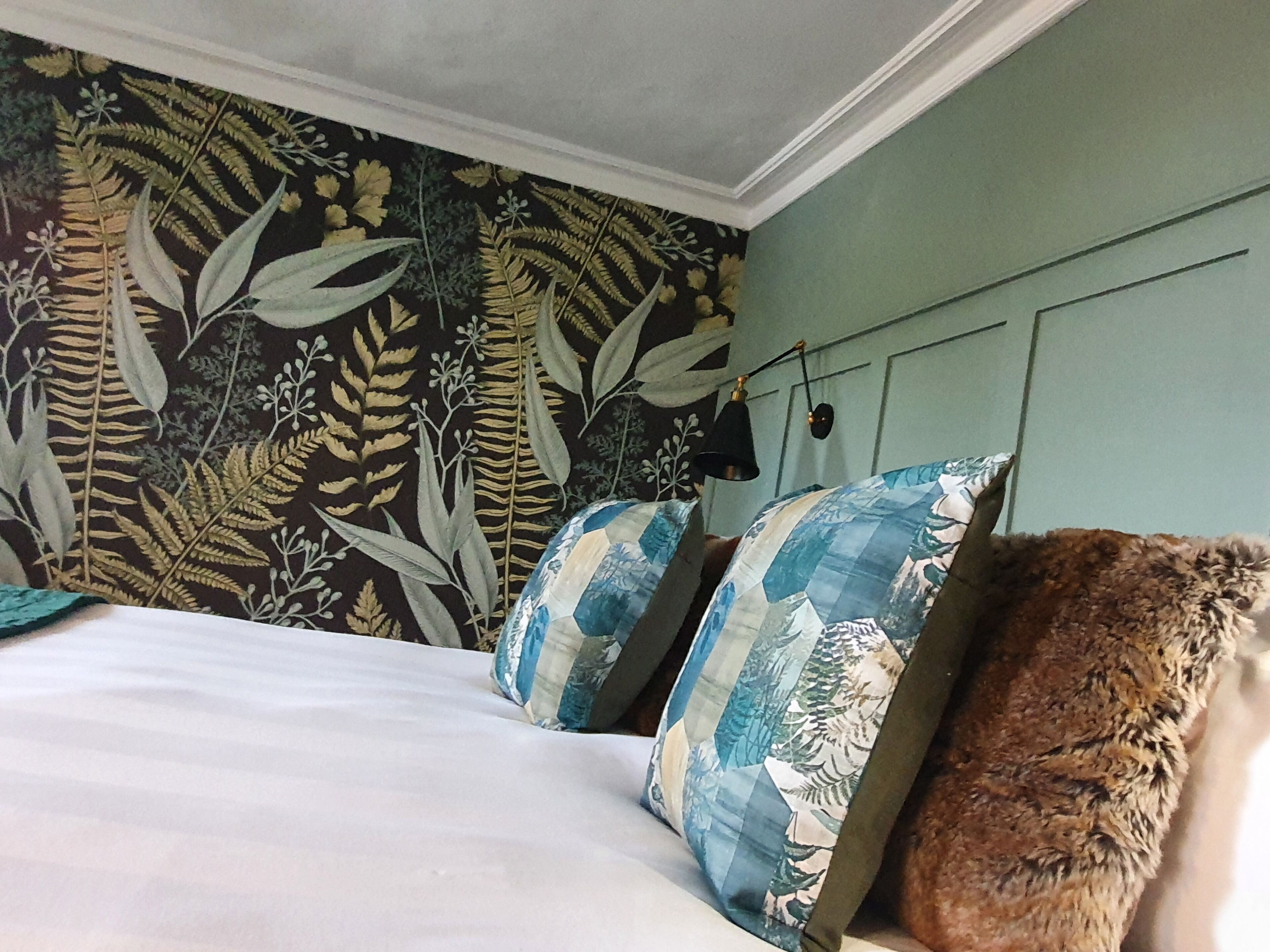 A bedroom with a bed, pillows, a wall with a leaf pattern, and a hanging lamp.